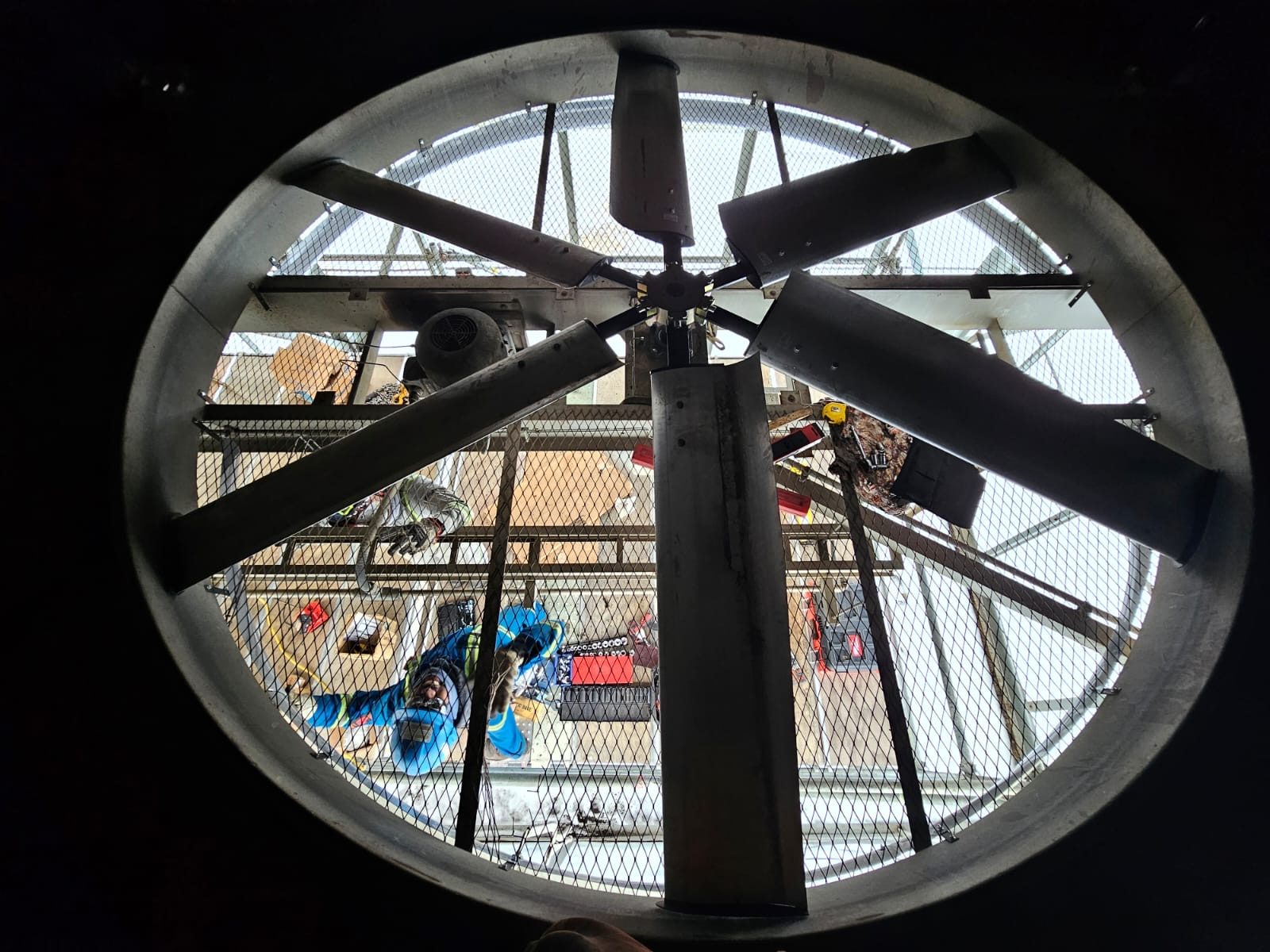 Looking up through an air cooler fan ring at a technician working on the fan below