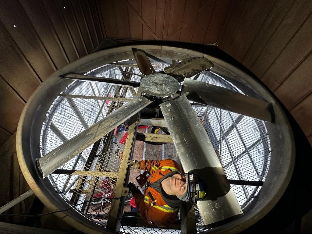 Technician in coveralls inspecting a six blade axial fan inside its fan ring